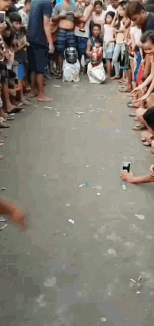 a crowd of people are gathered on the side of a road watching a person sitting on the ground .