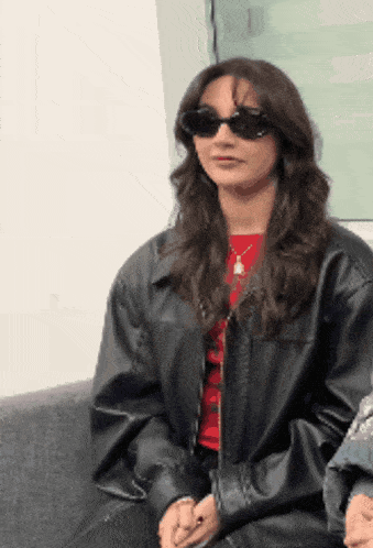 a woman wearing sunglasses and a black leather jacket is sitting on a couch