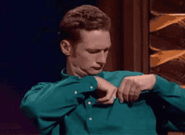 a man in a green shirt is adjusting his sleeve