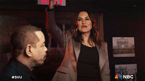 a man and a woman are standing in front of a red exit sign with the nbc logo on the bottom right