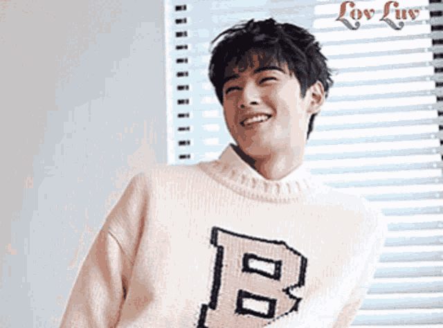 a young man wearing a sweater with the letter p on it is smiling in front of a window .