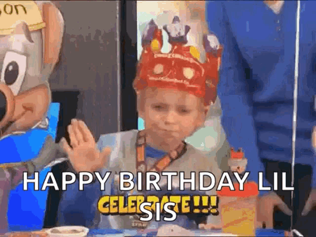 a little boy wearing a crown is sitting at a table with a chuck e cheese mascot behind him .