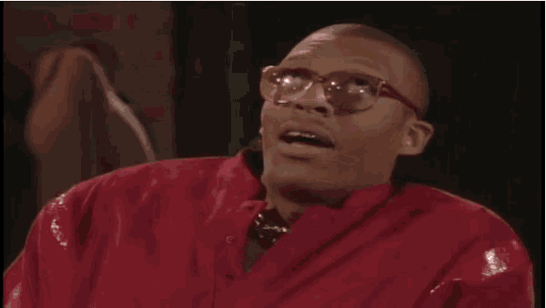 a man in a red jacket and glasses is making a funny face .