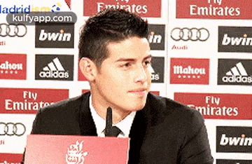 a man in a suit and tie is sitting in front of a sign that says fly emirates bwin and mahou