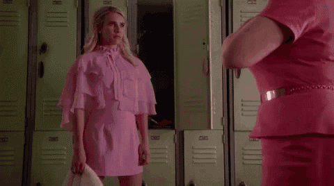 a woman in a pink dress is standing in a locker room talking to another woman .