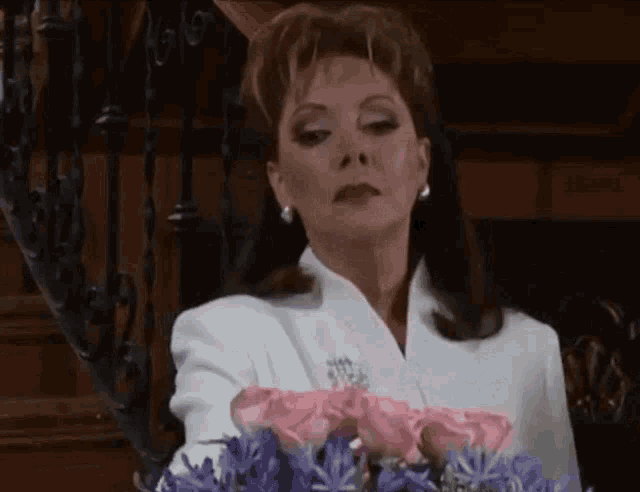 a woman in a white suit is holding a bouquet of pink roses .