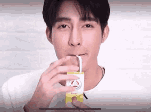 a young man is drinking a juice from a carton with a straw .