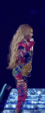a woman in a colorful outfit is standing on a stage with a microphone .