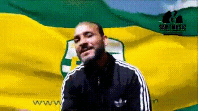 a man stands in front of a yellow and green flag with the words sabi music on it