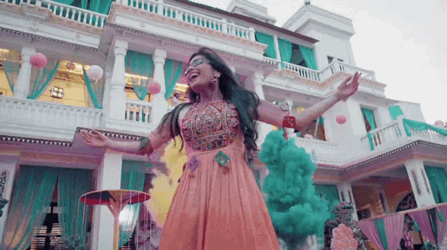 a woman in an orange dress is dancing in front of a large house