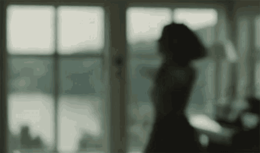 a blurry picture of a woman standing in front of a window looking out .