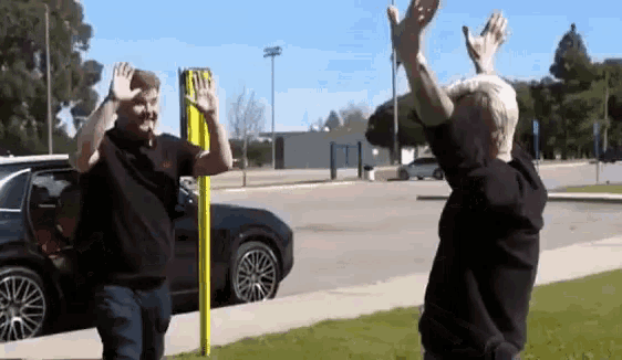 two men are waving at each other in front of a yellow sign that says no parking