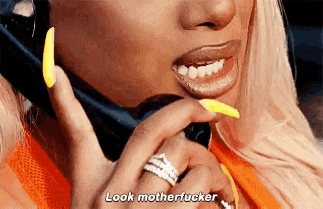 a woman with long yellow nails is talking on a cell phone and says look motherfucker .