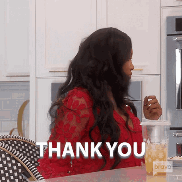 a woman in a red dress is sitting at a table with a cup of orange juice and says " thank you "