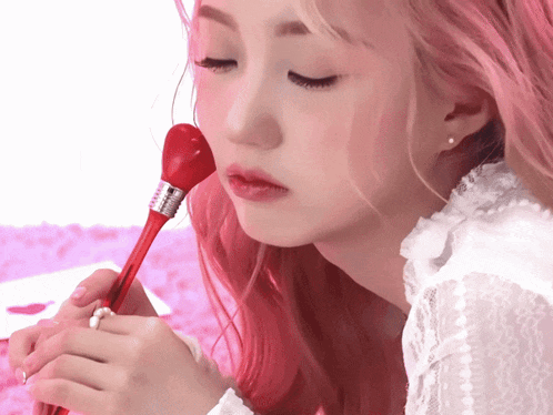 a woman with pink hair is holding a red heart shaped brush in her hand