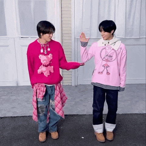 two young men are standing next to each other wearing pink sweaters and holding hands .