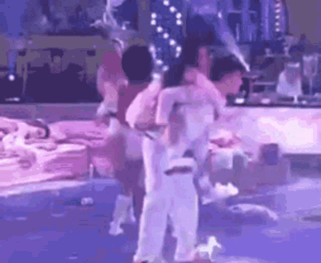 a group of people are dancing on a stage with purple lights .