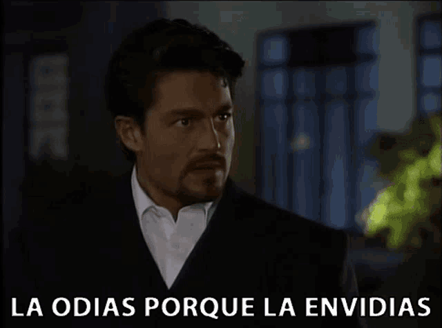 a man in a suit and white shirt is standing in front of a sign that says la odias porque la envidias