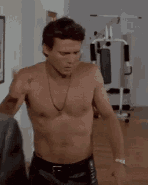 a shirtless man in leather pants is standing in a room with a necklace around his neck .