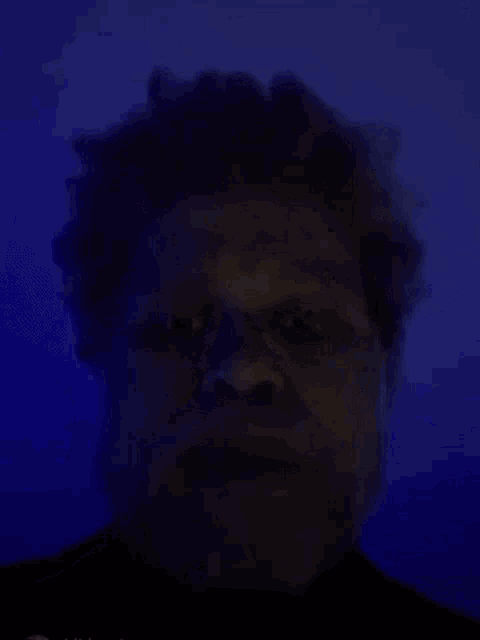 a man with a beard and curly hair is standing in front of a blue wall .