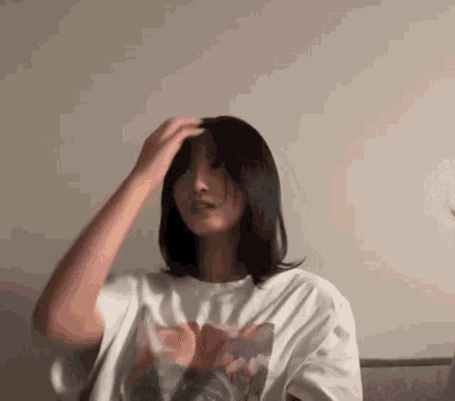 a woman in a white t-shirt is sitting on a couch and holding her hair .