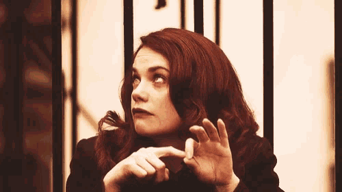 a woman with red hair is standing in front of a fence with her hands up .