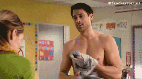 a shirtless man is talking to a woman in a classroom while holding a piece of paper .