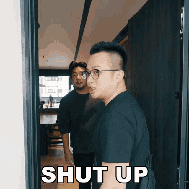 a man with glasses stands in front of a door with the words shut up above him