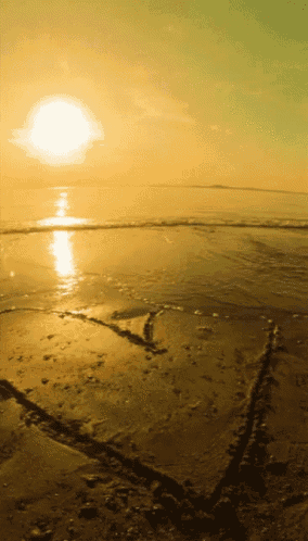 a sunset over a beach with a heart shaped drawing in the sand