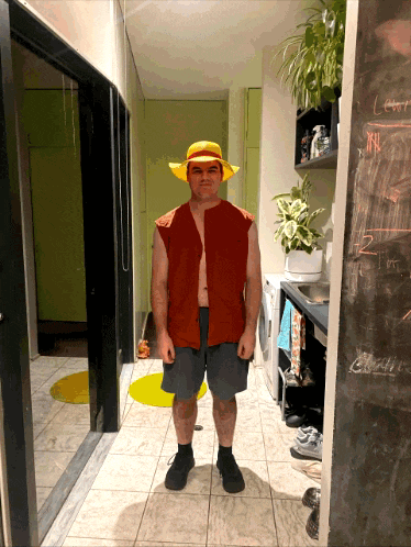a man standing in a hallway wearing a hat and a red vest