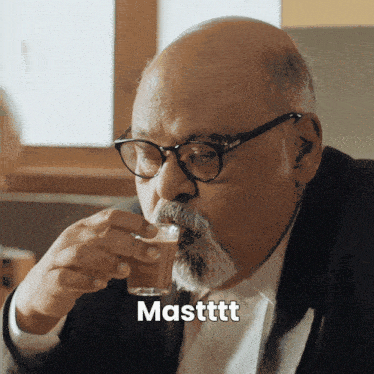 a man with glasses and a beard is drinking from a glass with the word masttt written below him