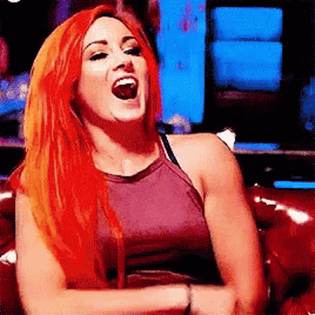a woman with red hair is sitting on a red couch and laughing