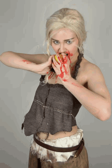a woman in a costume with blood on her face is eating an apple