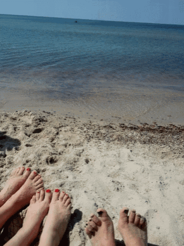 a group of people laying on a sandy beach with their feet painted red