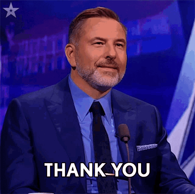 a man in a suit and tie is giving a thank you gesture