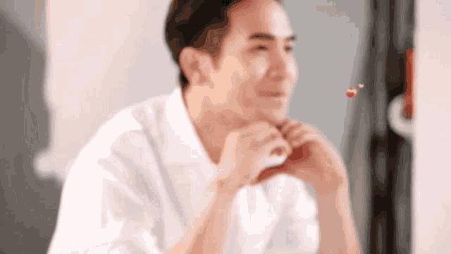 a man in a white shirt is making a heart shape with his hands .