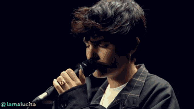 a young man is singing into a microphone with a ring on his finger