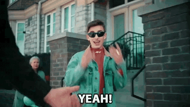 a young man wearing sunglasses says yeah in front of a building