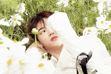 a man in a white shirt is laying in a field of flowers .