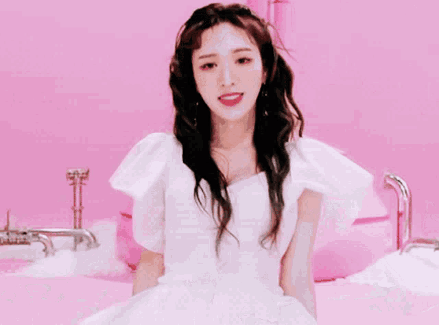 a woman wearing a white top and earrings is standing in front of a pink wall