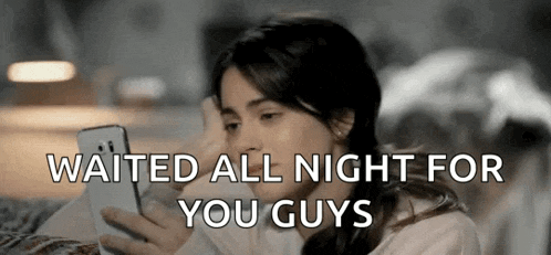 a woman is sitting on a couch looking at her phone with the words `` waited all night for you guys '' .