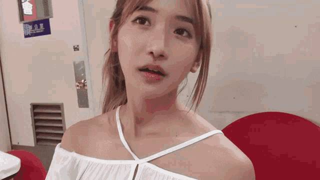 a woman in a white off the shoulder top stands in front of a red chair