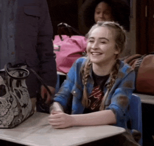 a young girl is sitting at a desk smiling .