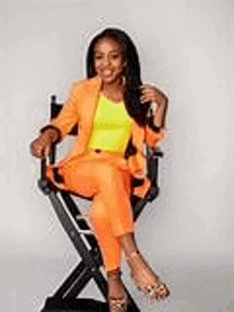 a woman is sitting in a director 's chair wearing an orange suit and a yellow shirt .