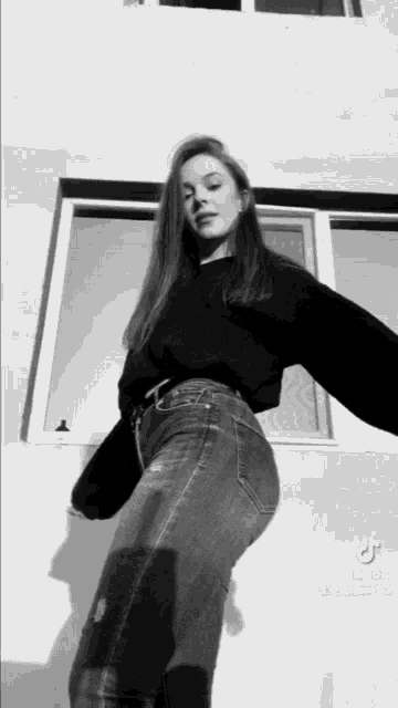 a woman wearing a black sweater and jeans is standing in front of a window .
