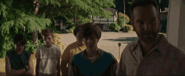 a group of boys are standing in front of a house with a man in a striped shirt