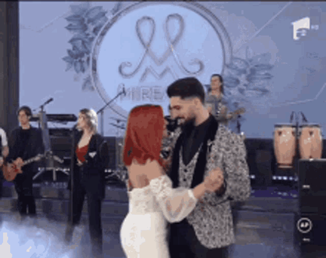 a man and a woman are dancing on a stage with a band behind them