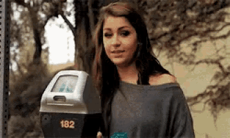 a woman is standing in front of a parking meter with the number 182 on it .