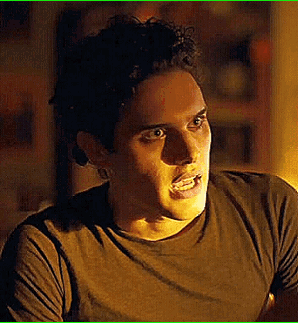a man in a brown t-shirt is making a funny face in a dark room .