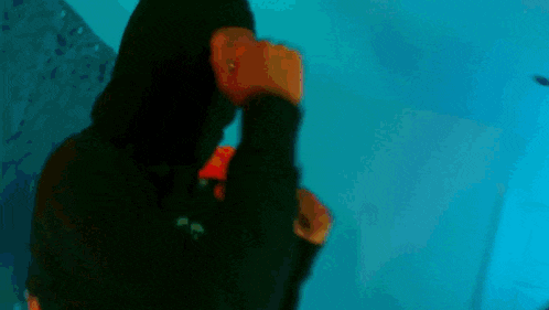 a young man is standing in a room wearing a black leather jacket and a red hoodie .